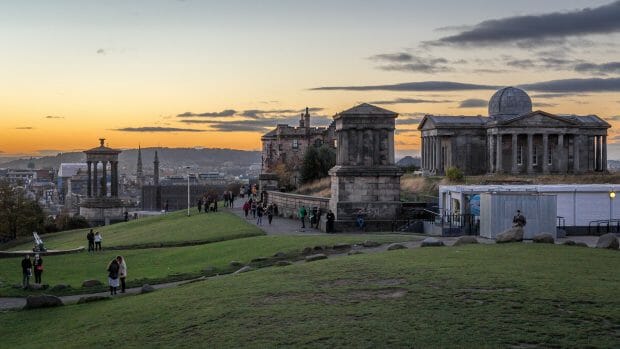 Auf dem Calton Hill von Edinburgh. In der Ferne ist ein oranger Streifen am Himmel zu sehen, die Sonne ist schon untergegangen. Rechts die Gebäude des Observatoriums.