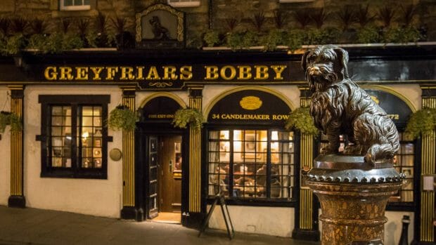 Die Bronzestatue des Hundes Greyfriar's Bobby vor dem gleichnamigen Pub bei Nacht.