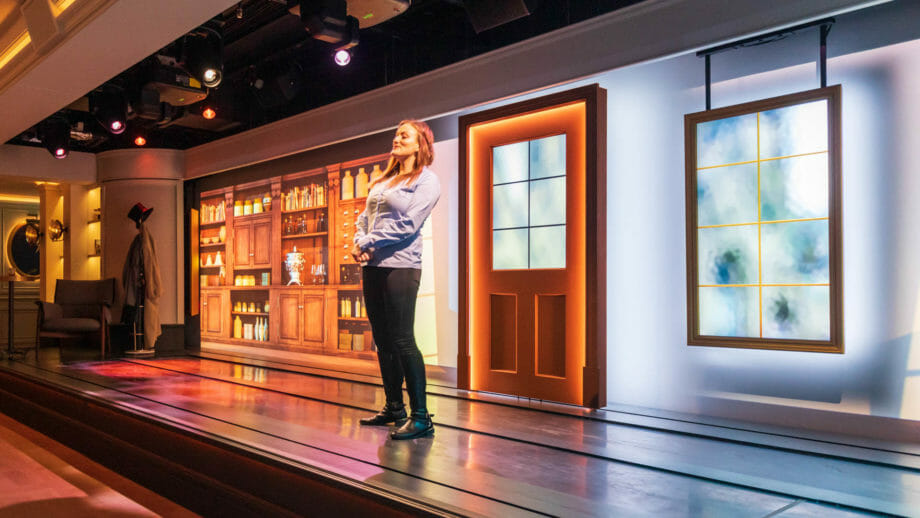 Eine Frau steht auf der Bühne in der Johnnie Walker Experience. Mit wechselnden Kulissen dahinter erzählt sie die Geschichte des Whisky-Machers.