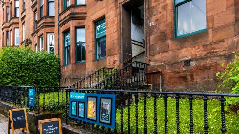 Eine Häuserfassade aus rotem Sandstein in Glasgow mit Schildern "National Trust for Scotland" und dem Schild "The Tenement House"