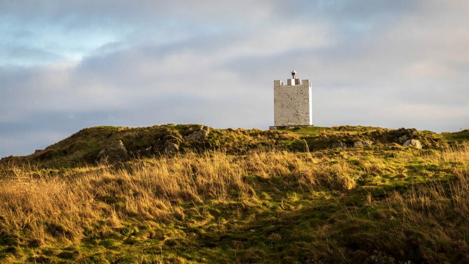 Ein weißer, eckiger, nicht allzu hoher Turm steht auf einem grünen Hügel. Das ist der Isle of Whithorn Tower.