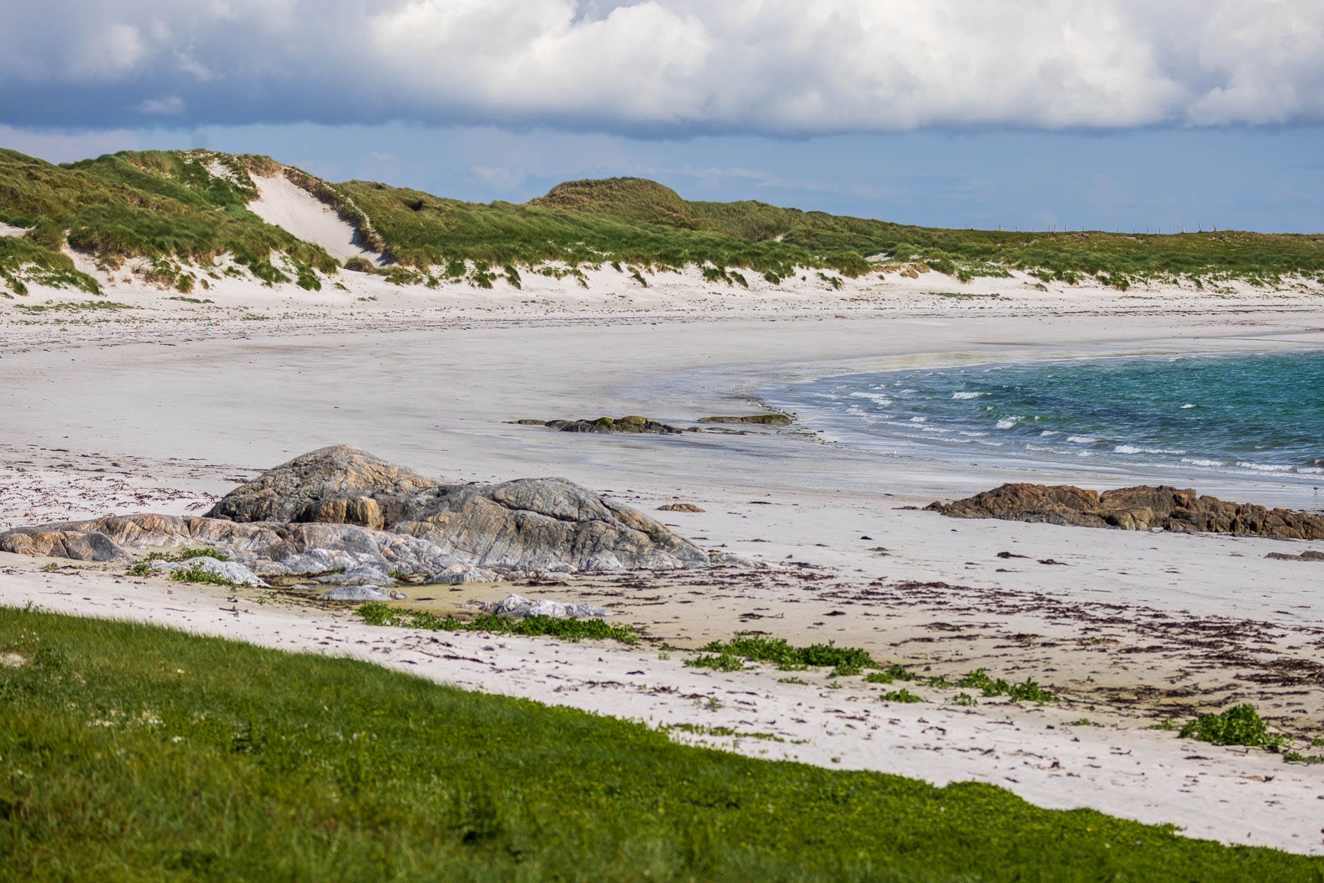 Ein weiter Sandstrand schwingt sich in einem Bogen am Meer entlang,