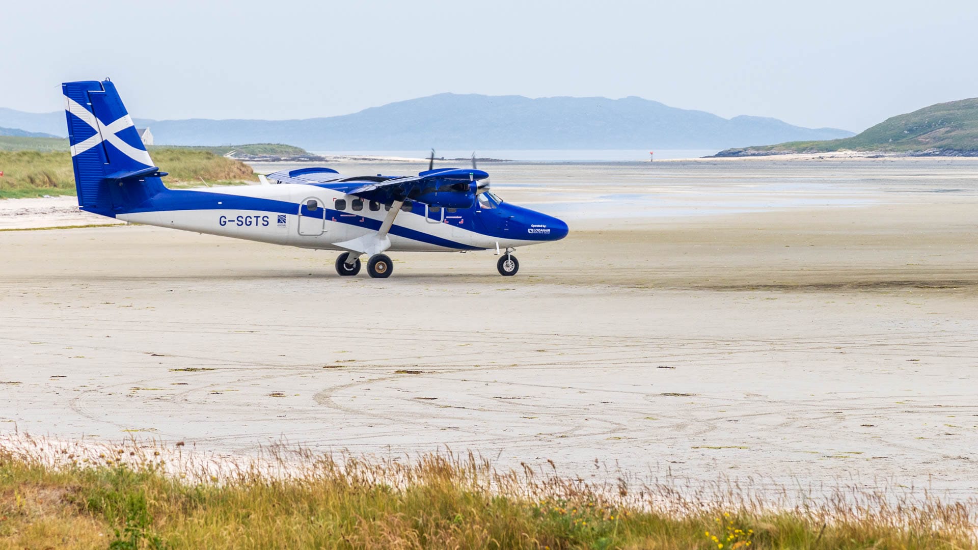 Ein blau-weißes Propeller-Flugzeug steht mit seinen drei Rädern auf einem riesigen Sandstrand.