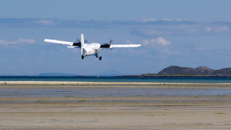 Ein weißes Propeller-Flugzeug hebt über einem Sandstrand ab