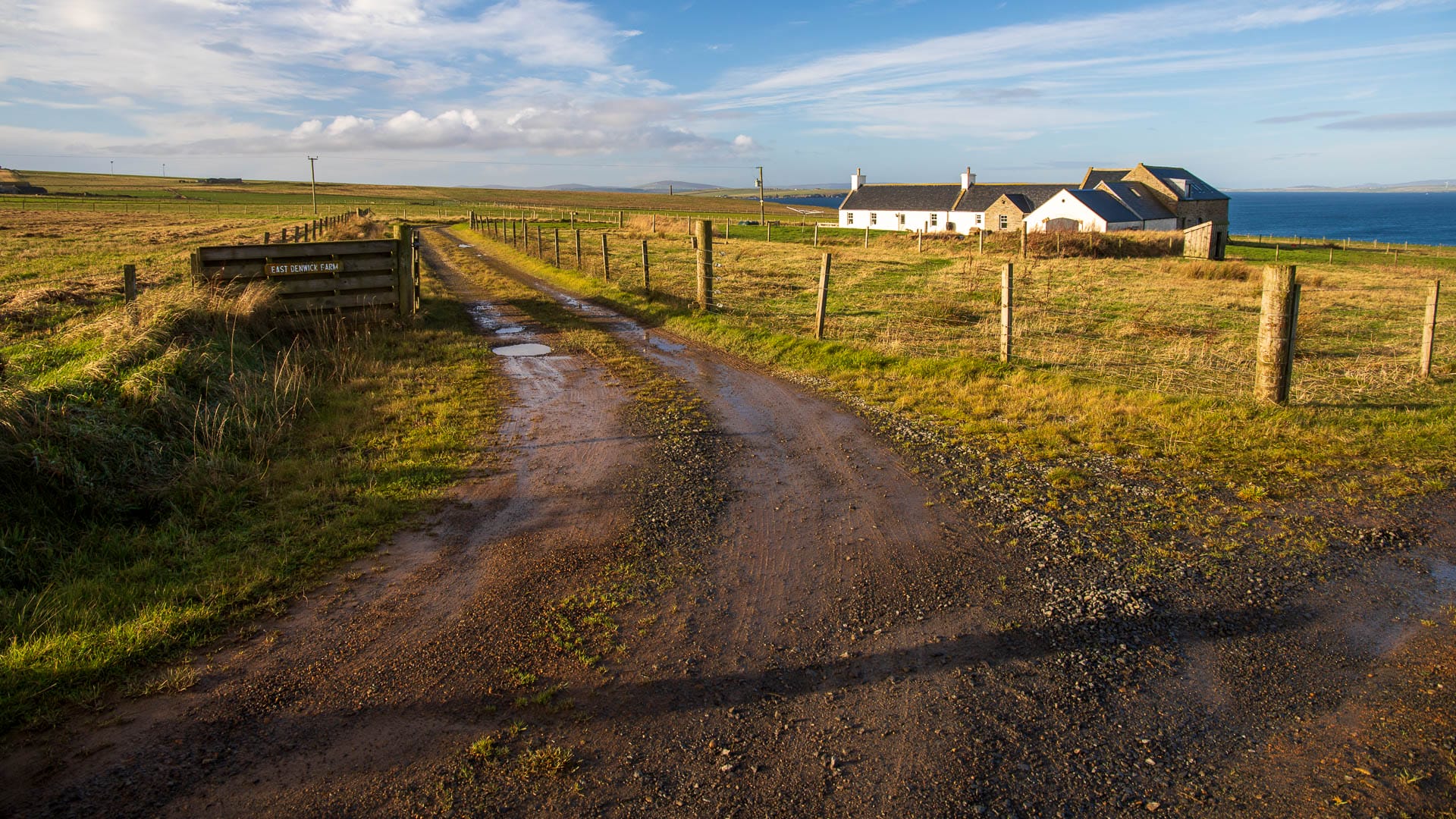 Ein schlammiger Feldweg und eine Farm im Hintergrund.