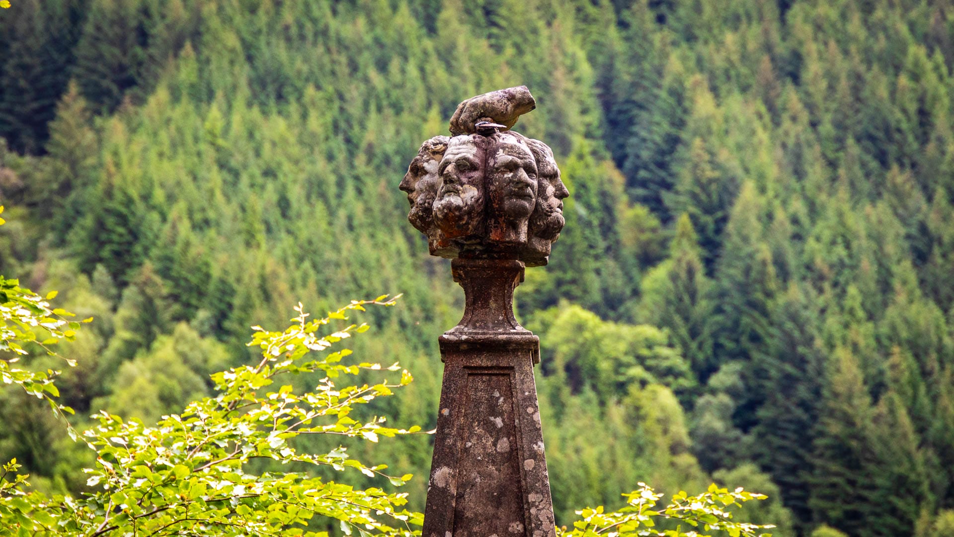 Die Spitze eines Denkmals mit aus Stein gemeißelten Köpfen und einer Hand mit einer Dolch darauf.