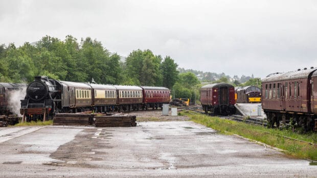 Der Jacobite Steam Train steht an einem Abstellplatz und dampft aus.