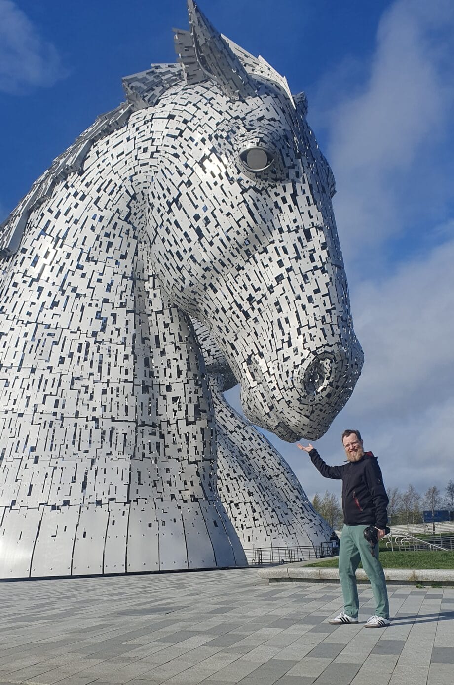 Ein Mann hält die Hand so unter den riesigen Pferde-Statuen hin, dass es durch die perspektivische Verzerrung so aussieht, als würde er sie füttern.