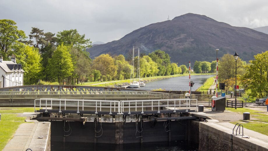 Blick auf eine Schleuse und eine Brücke des Caledonian Canal. Im Hintergrund ein Berg.