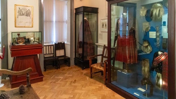 Ein Raum im West Highland Museum mit Vitrinen, in dem sich alte Kleidung wie Kilts befindet.